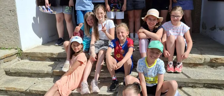 Eine Gruppe von Kindern und Jugendlichen posiert für ein Foto auf den Stufen eines Gebäudes. Sie lächeln und scheinen Spaß zu haben.