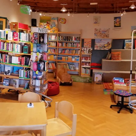 Ein kreisförmiger Raum mit Holzböden und Regalen voller Bücher, zusammen mit einigen Beanbags und einem Schreibtisch. Der Raum hat eine Holzdecke mit hängenden Lampen.