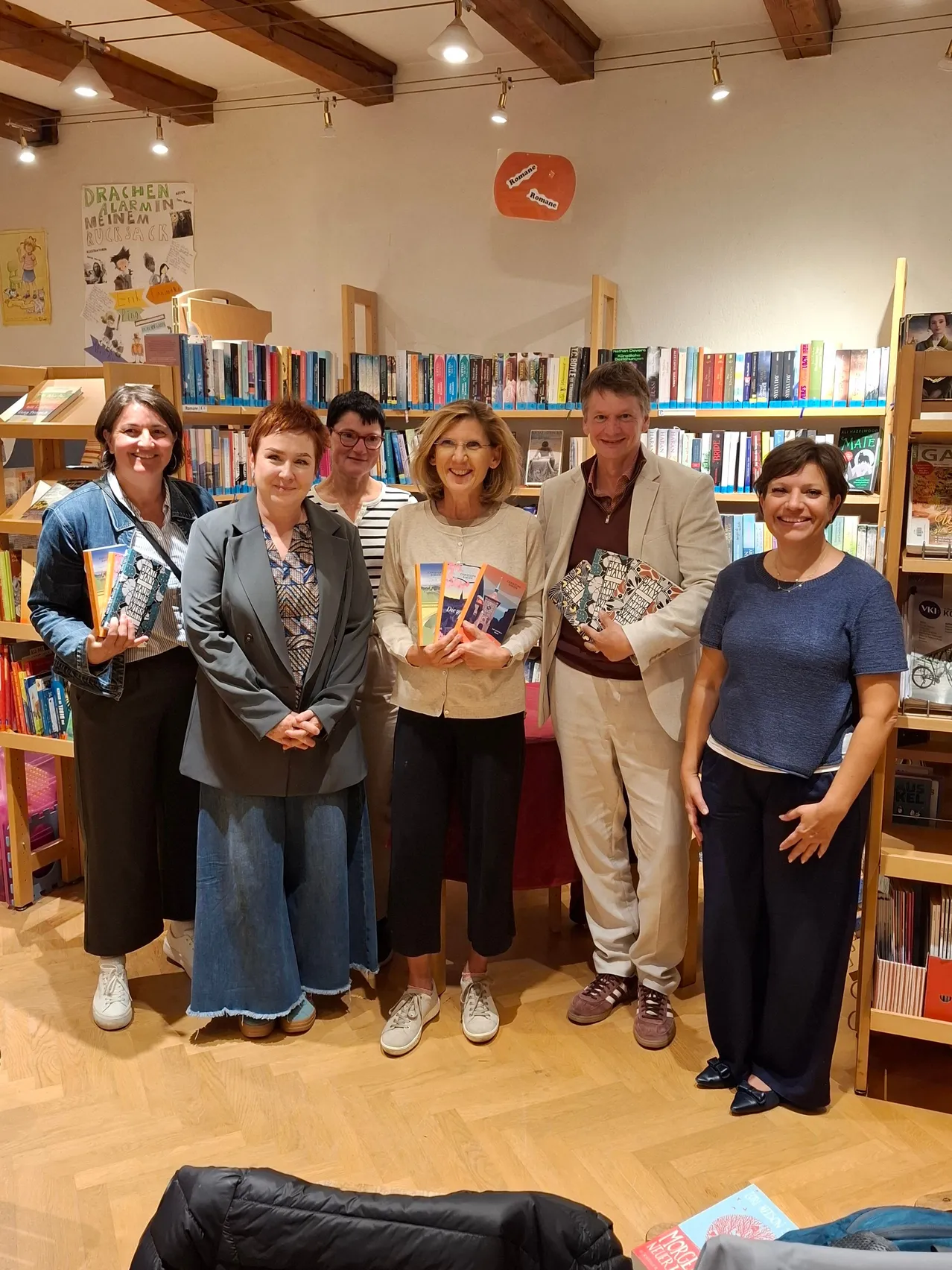 Eine Gruppe von Menschen steht in einer Buchhandlung, lächelt und hält Bücher. Sie posieren für ein Foto.
