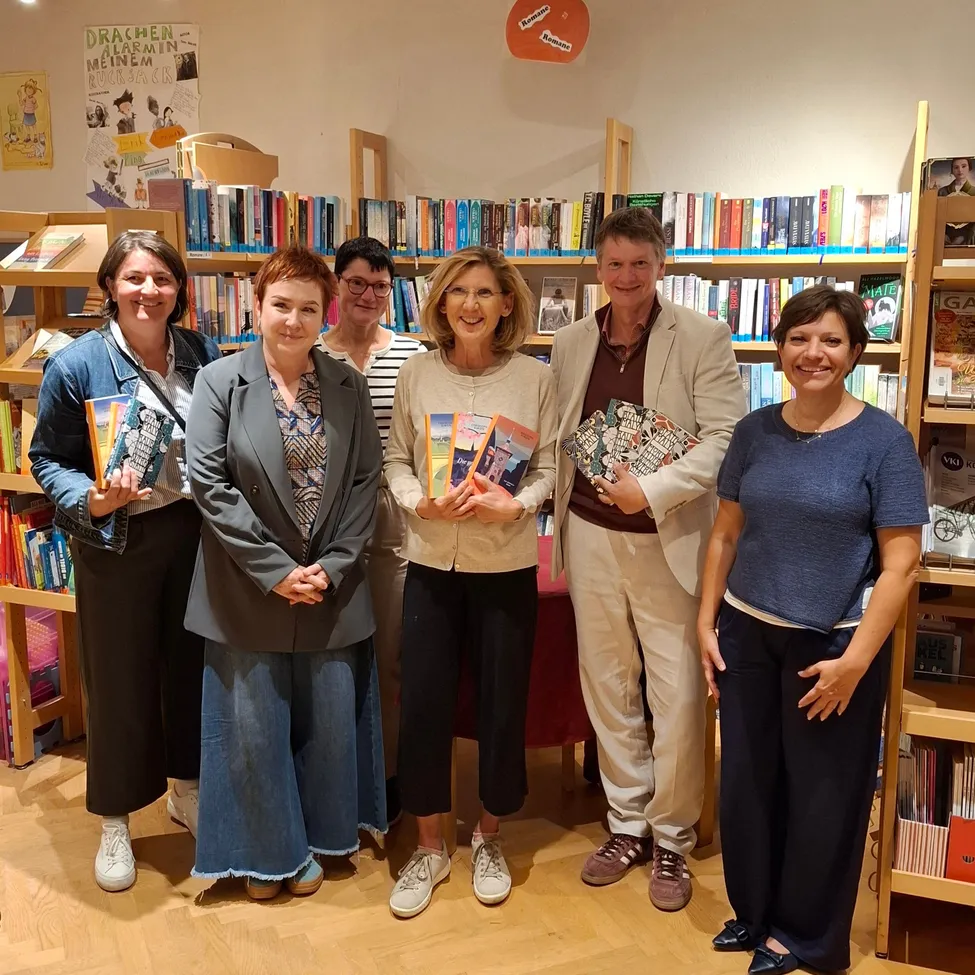 Eine Gruppe von Menschen steht in einer Buchhandlung, lächelt und hält Bücher. Sie posieren für ein Foto.