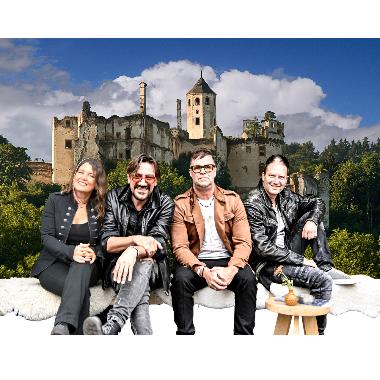 Four people are sitting on a white fur rug in front of a castle with a cloudy sky in the background.