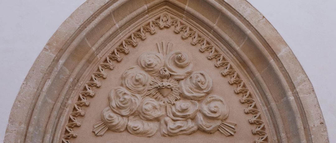 Ein Nahaufnahme eines kunstvollen Steinbogens mit aufwendigen Blumendesigns, mit einem Herz und einer Sonne in der Mitte, vor einem schlichten Hintergrund.