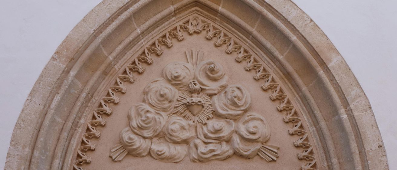 Ein Nahaufnahme eines kunstvollen Steinbogens mit aufwendigen Blumendesigns, mit einem Herz und einer Sonne in der Mitte, vor einem schlichten Hintergrund.