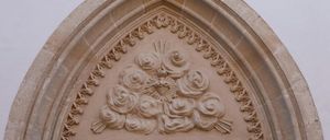 Ein Nahaufnahme eines kunstvollen Steinbogens mit aufwendigen Blumendesigns, mit einem Herz und einer Sonne in der Mitte, vor einem schlichten Hintergrund.