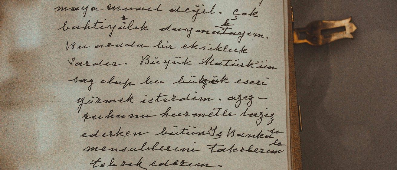 Eine handgeschriebene Notiz auf einem alten Stück Papier, datiert auf 1946, enthält kursiven Text in einer unbekannten Sprache, möglicherweise Türkisch. Das Papier ist gelblich und hat einen metallischen Schloss auf der Seite.