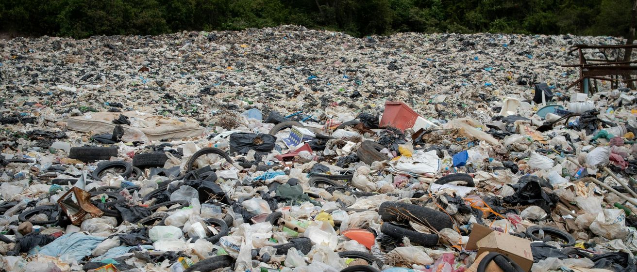 Eine Mülldeponie, gefüllt mit verschiedenen Abfallmaterialien, einschließlich Plastik, Gummi und anderem Schutt, umgeben von einem Wald.