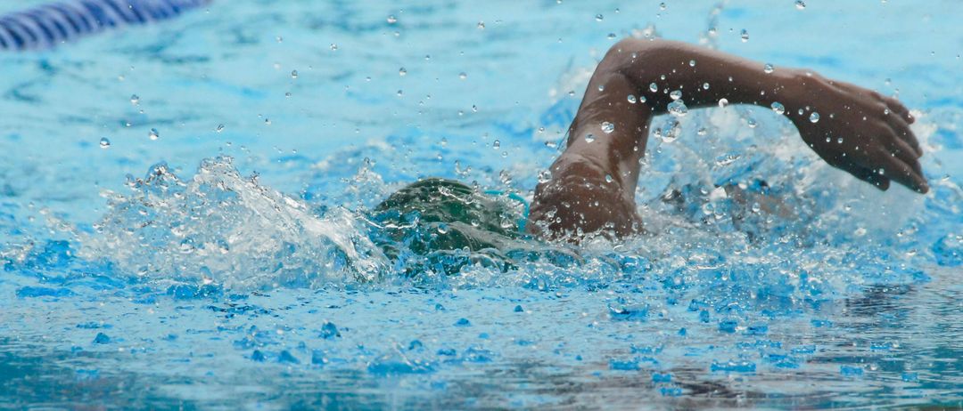 Eine Person schwimmt in einem Pool mit einem blauen Bahnseil und verursacht Wasserspritzer. Der Arm der Person ist ausgestreckt, und die Wassertropfen reflektieren das Licht.