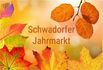 Ein Hintergrund aus Herbstblättern mit den Worten Schwadorfer Jahrmarkt in der Mitte. Die Blätter sind in Gelb-, Orange- und Rottönen gehalten.