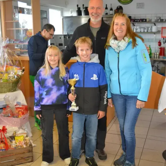 Eine Familie mit zwei Kindern und einem Mann posiert für ein Foto in einem Raum mit Geschenken und Trophäen.