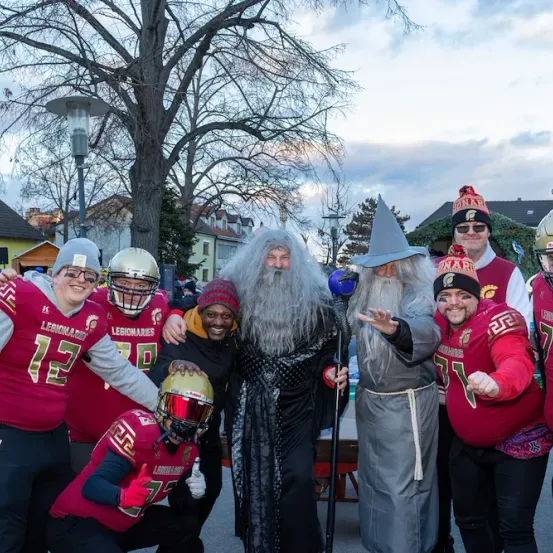 Eine Gruppe von Footballspielern in roten Trikots posiert für ein Foto mit Gandalf und einem Zauberer bei einer Outdoor-Veranstaltung.