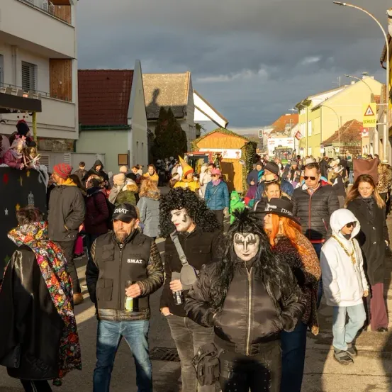 Eine überfüllte Straße mit Menschen in verschiedenen Kostümen. Einige tragen Schminke im Gesicht und manche haben Handtaschen. Gebäude und Straßenlaternen säumen die Straßenseite.