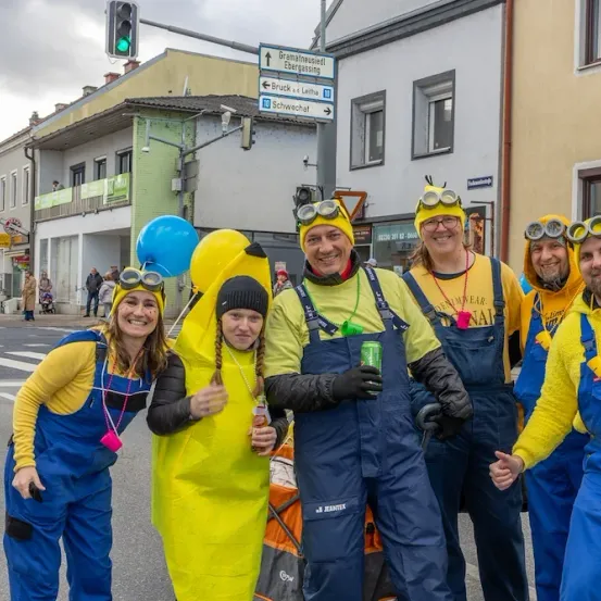 Eine Gruppe von Menschen, die als Minions verkleidet sind, posiert für ein Foto auf einer Straße mit Luftballons und Gebäuden.