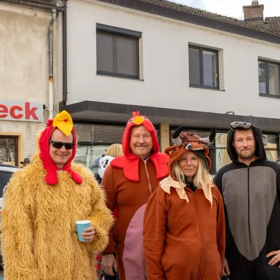 Vier Menschen in Tierkostümen posieren für ein Foto vor einem Gebäude. Einer hält einen blauen Becher. Ein Auto ist in der Nähe geparkt.