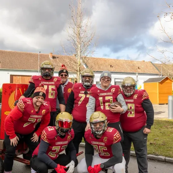 Eine Gruppe von Footballspielern in roten Trikots mit den Nummern 7, 12, 27, 6, 76 und 9, posiert für ein Foto vor Häusern.