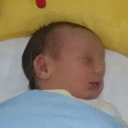 Ein Baby schläft friedlich auf einem Bett mit einer gelben Decke und trägt eine blaue Decke.