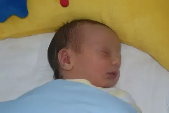 Ein Baby schläft friedlich auf einem Bett mit einer gelben Decke und trägt eine blaue Decke.