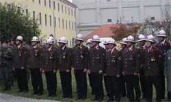 Eine Gruppe uniformierter Männer in Hüten und Medaillen steht in einer Reihe auf dem Rasen vor einem Gebäude mit vielen Fenstern.