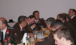 Eine Gruppe von Militäroffizieren in Uniform sitzt um einen Tisch herum und genießt Getränke und Essen. Sie scheinen sich in einer Besprechung oder einem formellen Treffen zu befinden.