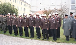 Eine Gruppe uniformierter Personen, möglicherweise Militärangehörige, steht auf einem Rasen vor einem Gebäude, einige tragen Hüte und Schuhe.