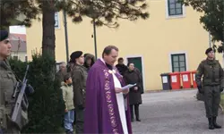 Ein Mann in einem violetten Gewand liest von einem Papier, der sich neben einem Baum befindet, wobei ein Militäroffizier rechts und ein Soldat mit einer Waffe links stehen.