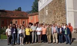 Eine Gruppe von Menschen in Freizeitkleidung steht vor einem alten Gebäude mit einer Steinmauer. Das Gebäude hat mehrere Fenster und ein rotes Dach. Die Gruppe scheint für ein Foto zu posieren.