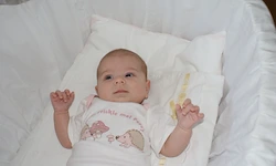 Ein Baby in einem weißen Shirt liegt in einem Kinderbett mit einem weißen Kissen und einer weißen Decke.