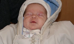 Ein Baby schläft und trägt eine weiße und blaue Kapuzenjacke. Das Baby ist in eine weiße Decke gehüllt.