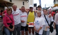 Eine Gruppe von Menschen, wahrscheinlich ein Laufteam, posiert für ein Foto mit einem verschwommenen Hintergrund. Sie tragen passende weiße Shirts und Nummern, wobei ein Mann ein gelbes Shirt trägt.