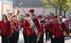 Ein Musikverein in roten Uniformen und Mützen spielt verschiedene Musikinstrumente, während er die Straße entlanggeht.