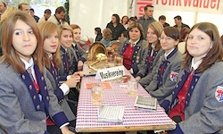 Eine Gruppe junger Frauen in Uniformen sitzt um einen Tisch herum mit einem Pokal und verschiedenen Gegenständen, wahrscheinlich bei einer Veranstaltung oder Versammlung.