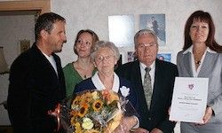 Eine Gruppe von Menschen steht zusammen, eine Frau hält einen Strauß Sonnenblumen und eine andere ein Zertifikat. Sie lächeln für ein Foto.
