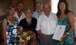Eine Gruppe von Menschen steht in einem Raum. Eine Frau hält ein Papier und einen Blumenstrauß. Sie posieren für ein Foto.