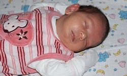 Ein Baby in einem rosa und weißen gestreiften Strampler schläft friedlich auf einer bunten Decke mit einem Teddybären und Mond.