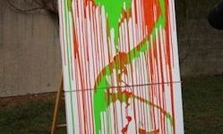Ein großes Leinen mit lebhaften, abstrakten Farbspuren in Rot, Grün und Weiß steht auf einem Rasen vor einer beigen Wand.