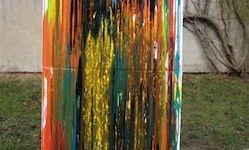 Ein abstraktes Gemälde mit leuchtenden Farben, darunter Rot, Gelb, Blau und Grün, steht vor einem Hintergrund aus Beton und Grün.