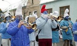 Eine Gruppe von Menschen in blauen Kostümen und weißen Mützen spielt Musikinstrumente bei einem Umzug im Freien.