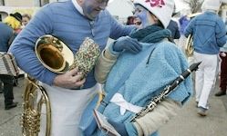 Zwei Musiker in blauer und weißer Kleidung stehen draußen. Einer hält eine Tuba und der andere eine Klarinette. Sie nehmen wahrscheinlich an einer Parade teil.