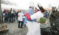 Eine Gruppe von Menschen in Kochuniformen feiert an einem verschneiten Außenbereich, während einige Zuschauer und Kinder zusehen.