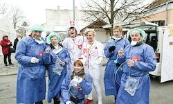 Eine Gruppe von Menschen, die blaue Arztkittel und grüne Kappen tragen, posiert für ein Foto vor einem Van.