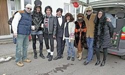 Eine Gruppe von Menschen in verschiedenen Kostümen steht draußen, lächelt und posiert für ein Foto vor einem Van.