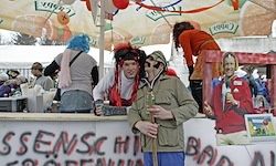 Menschen stehen hinter einem Tresen mit einem Schild, das 'Sense Hi' und 'Bad Food' sagt. Einige sind in Kostümen gekleidet. Eine Frau steht auf einem Stuhl.