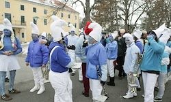 Eine Gruppe von Menschen in blauen und weißen Kostümen und weißen Hüten spielt Musikinstrumente auf der Straße. Einige von ihnen halten Trompeten.
