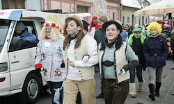 Eine Gruppe von Menschen in Kostümen geht die Straße entlang, mit einem weißen Van am Straßenrand geparkt. Sie tragen alle Hüte und Stiefel.