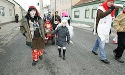 Eine Gruppe von Menschen geht tagsüber auf einer Straße. Einige tragen Kostüme und Masken, und es gibt Gebäude an der Seite.