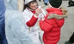Eine Frau in einer roten und weißen Kleidung hält ein kleines Objekt in ihren Händen und spricht mit einem Kind in einer roten, flauschigen Jacke im Freien.