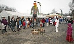 Eine Menschenmenge steht um eine große, bunte Figur, die von einer Metallstruktur aufgehängt wird, mit Zelten und einem verschneiten Hintergrund.