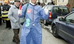 Ein Mann in einem blauen Schutzanzug hält eine rote Flagge auf einer Straße mit geparkten Autos und Menschen im Hintergrund.