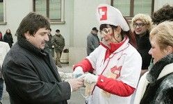 Ein Mann und eine Frau tauschen Gegenstände aus; eine Person in einer Krankenschwester-Uniform ist in der Nähe. Eine Menschenmenge ist im Hintergrund, und ein Mann ist in militärischer Kleidung.