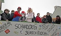 Eine Gruppe von Menschen in Kostümen, möglicherweise bei einem Karneval, steht hinter einem Banner mit den Worten Schwadorfer Borsen Krocach, mit verschiedenen Aufklebern und dem Euro-Symbol.