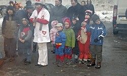 Eine Gruppe von Kindern und Erwachsenen steht in einer Reihe auf einer verschneiten Straße. Ein Erwachsener in einem weißen Mantel führt sie an.